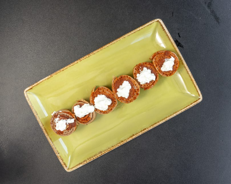 Seven rolled pancakes with white cream filling arranged diagonally on a light green rectangular plate.