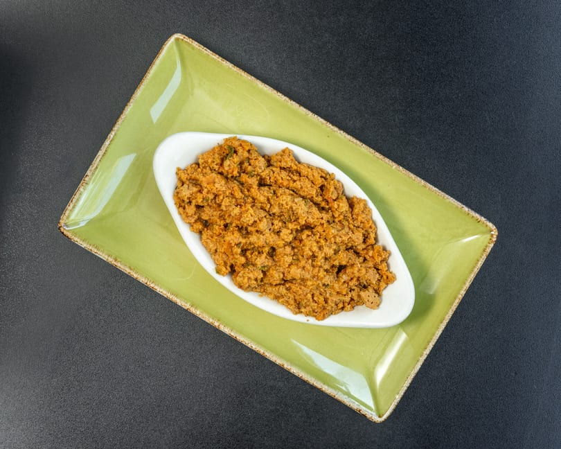 A white oval dish filled with a savory, textured orange-brown meat mixture, on a green rectangular plate.