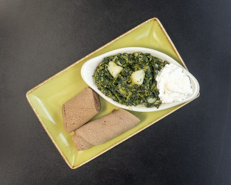 Ethiopian Gomen, collard greens with potatoes and cheese, served with injera on a green plate.