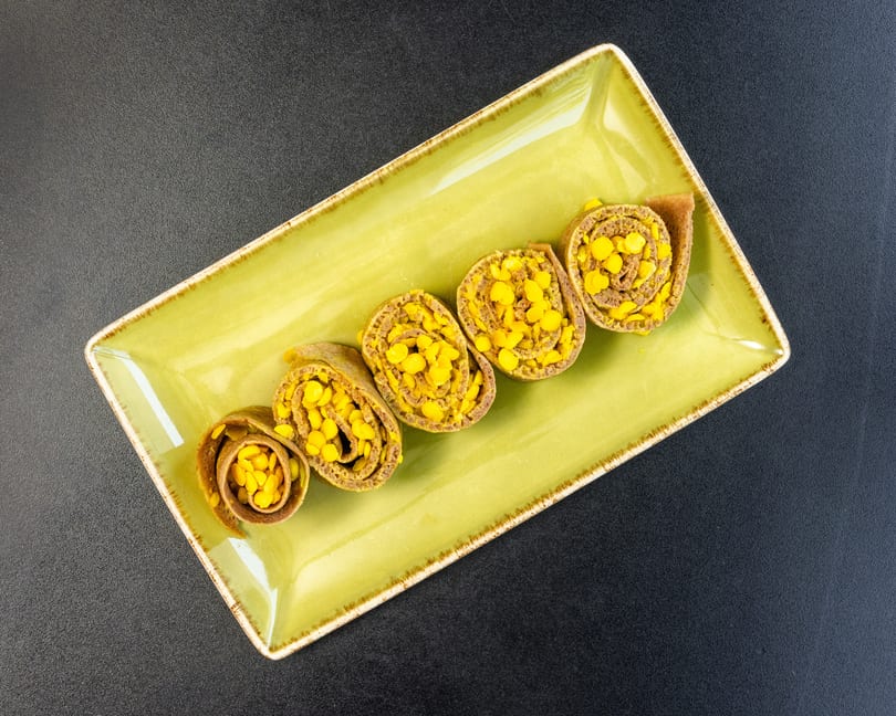 Five corn-filled crepes, rolled and sliced, arranged on a rectangular green plate.