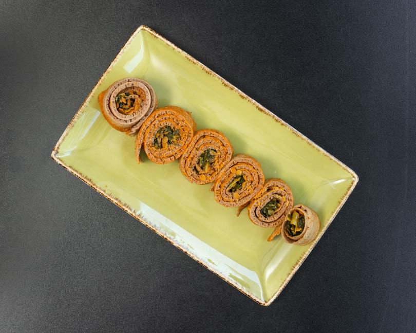 Savory crepes filled with orange spread and green vegetables, arranged on a light green rectangular plate.
