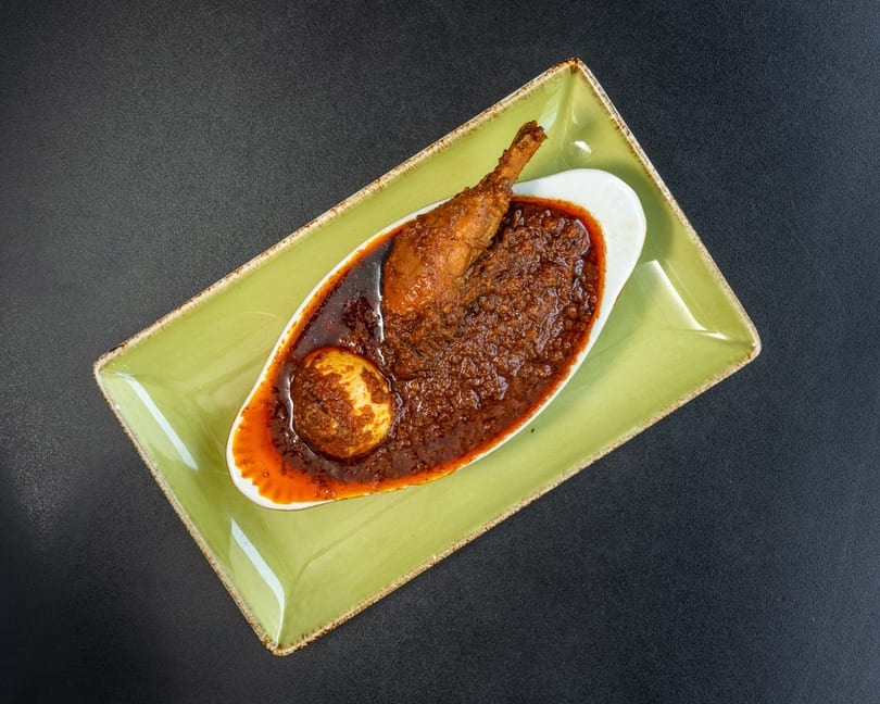 Chicken drumstick and a hard-boiled egg in a rich, dark red sauce, served on a green plate.