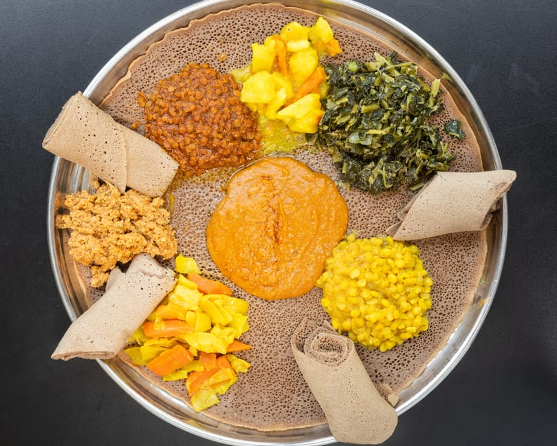 Overhead view of a large platter of Ethiopian food with injera bread and various colorful stews.