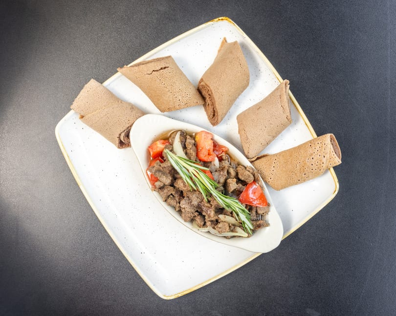 Ethiopian tibs, a meat dish with tomatoes, onions, and rosemary, served with injera bread.